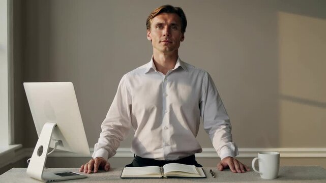 Confident businessman sitting at desk with open notebook and computer