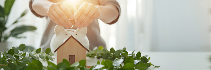 Close-up of a hand holding a coin, a house model, a piggy bank in a room
