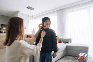 Fototapeta premium Child prepares to go outside while adult helps with winter clothing in a bright living room in the morning