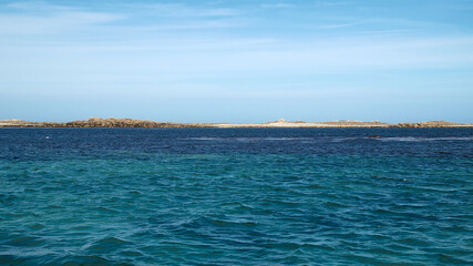 Obraz premium Distant coastline and calm sea beneath a blue sky on the horizon, creating a peaceful and open coastal landscape.