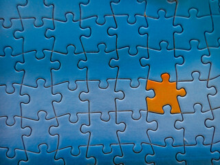 Close up of blue puzzle pieces put together with one in orange that looks like a person
