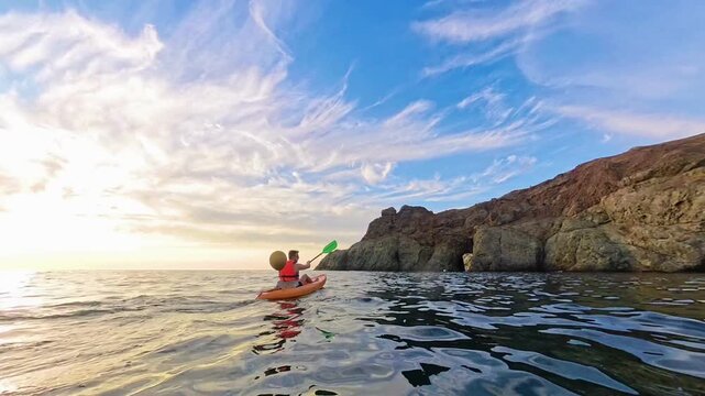 Kayaking sunset ocean man paddles a kayak along a rugged rocky coastline during a peaceful golden hour for summer adventure