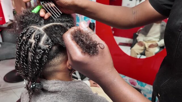 Rear-side view of stylist using a fine-tooth comb to section afro hair, teen boy blurred in mirror reflection