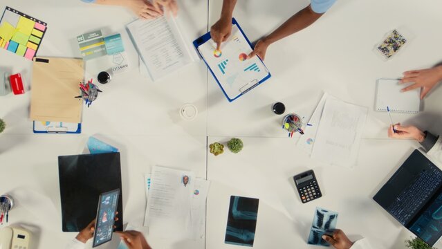 Top down view of experts group reviewing clinical data, working together and sharing their expertise to improve healthcare services at the hospital. Brainstorm treatment ideas.