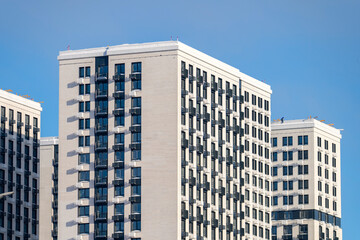 A tall building with a lot of windows and a white roof. The building is surrounded by other buildings