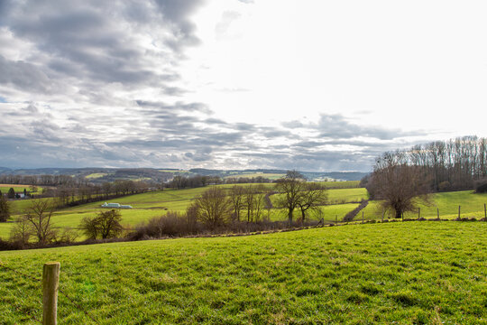 Rolling hills with farm fields, leafless trees and a dramatic sky in the background.