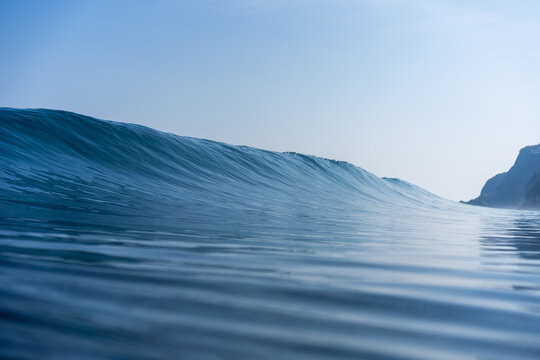 Water level view of a clean blue ocean wave forming smooth lines across the surface with soft light and open horizon.