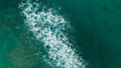 Aerial top down view of ocean waves breaking over shallow coral reef creating white foam patterns in turquoise tropical water. © Bpato Media