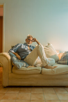 Stylish mature man with silver hair relaxing on a sofa in a bright living room