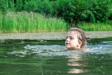 Fototapeta premium Schoolgirl learns to swim at a village pond during summer holidays. Swimming lessons