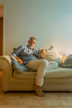 Stylish mature man with silver hair relaxing on a sofa in a bright living room