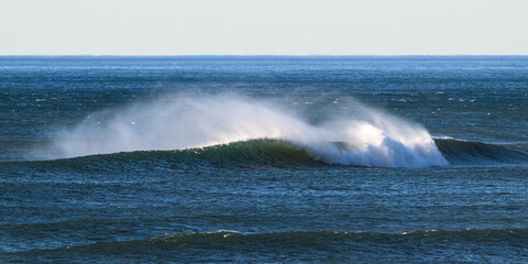 Naklejka premium Ocean wave blown by strong wind pulling spray away from the crest towards horizon