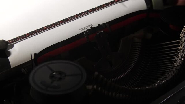 Vintage mechanical typewriter typing the word hollywood onto a sheet of white paper, representing screenwriting, storytelling, and the golden age of cinema