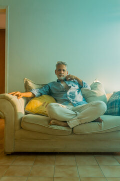 Stylish mature man with silver hair relaxing on a sofa in a bright living room