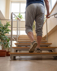 Fototapeta premium Rear View of Man Climbing Stairs Holding Handrail During Physical Therapy Rehabilitation