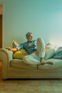 Stylish mature man with silver hair relaxing on a sofa in a bright living room