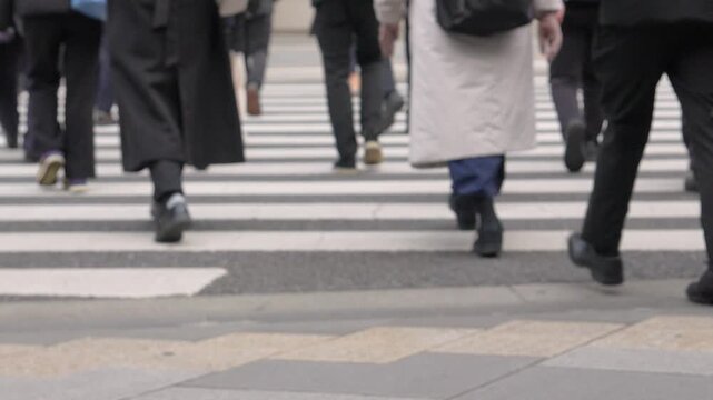 Slow-motion and Low‑angle footage of pedestrians&rsquo; legs crossing an urban crosswalk, intentionally blurred.
