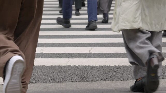 Slow-motion and Low‑angle footage of pedestrians&rsquo; legs crossing an urban crosswalk.