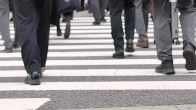 Slow-motion and Low‑angle footage of pedestrians&rsquo; legs crossing an urban crosswalk, intentionally blurred.
