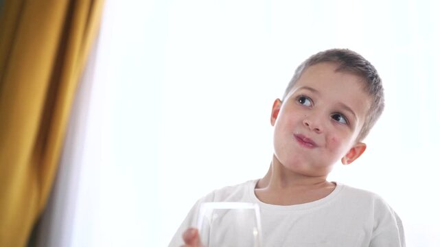 Young boy holding glass of water. Young boy drinks water from glass. A child is drinking a glass of water. A little boy with a lifestyle glass of water.