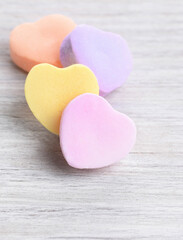 Obraz premium Closeup with shallow depth of field of 4 pastel Valentine's Day heart shaped candies on a white wood surface.