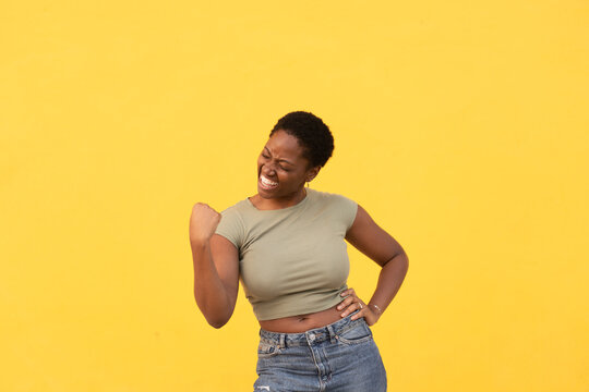 Excited woman clenching fist to celebrate success against yellow background. Lady in casual clothes showing joyful expression and confident gesture