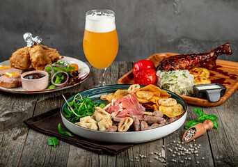 Food spread with drinks at a dining table during a casual gathering. Different dishes and drinks are placed on a wooden table during a casual meal. Food includes meats, salads, and snacks.