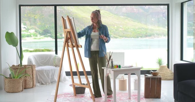 Artist is starting painting at easel dipping brush into paint and adding marks and checking layout