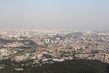 Obraz premium Panoramic aerial view of a sprawling metropolis with dense residential areas and high-rise buildings under a hazy sky - Vista aérea panorâmica de uma metrópole com áreas residenciais densas e edifício