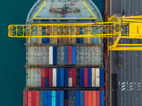 Aerial view of a cargo ship loaded with colorful containers contrasting against the deep blue sea, docked in the port, Trieste, Italy.