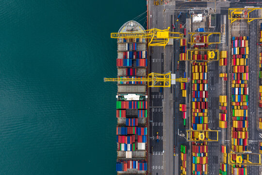 Aerial view of a vibrant tapestry of stacked containers contrasting sharply against the deep blue sea at the bustling port, Trieste, Italy.