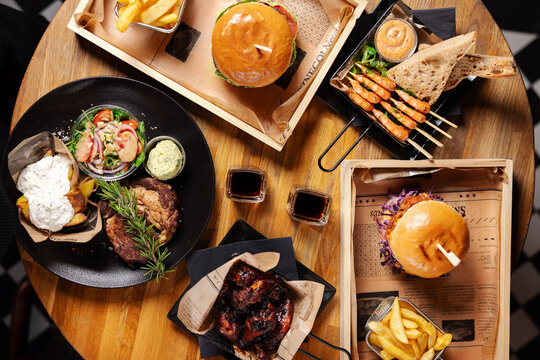 Restaurant table with burgers, steak and shared dishes
Sharing food at a restaurant table with meat and sides
Group dinner with burgers and steak served for sharing
