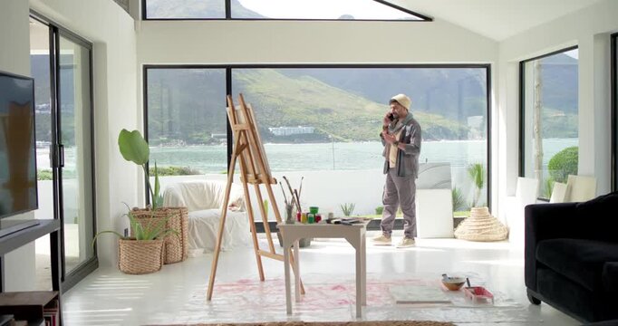 Indian man pacing on phone after receiving call, discussing commission near easel, copy space