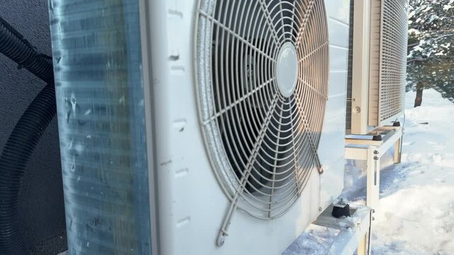 Side View of Heat Pump with Iced Feet. A side view shows a white heat pump with ice encasing its rubber mounting feet, sunlit against the frozen base.