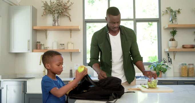 African American father and son packing snacks into black backpack for school at kitchen island