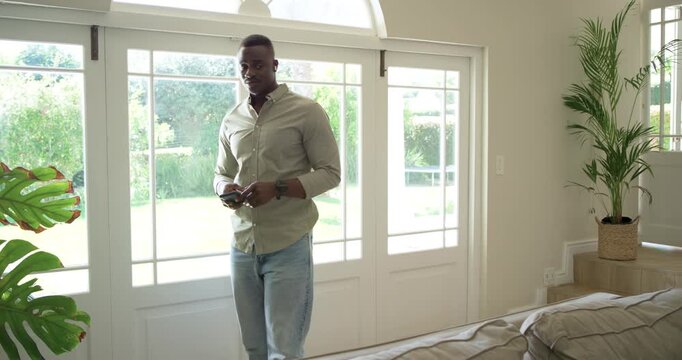 African American mid-adult man entering living room, holding phone and sunglasses, checking yard