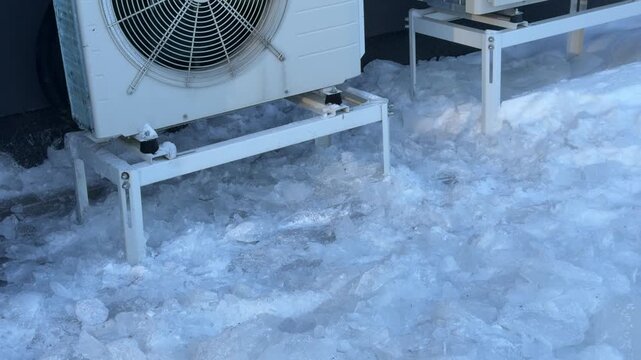 Ground Level View of Ice Chunks Under Heat Pumps. A low-angle view shows shattered ice chunks covering the ground beneath heat pump stands, depicting the aftermath of ice clearing.