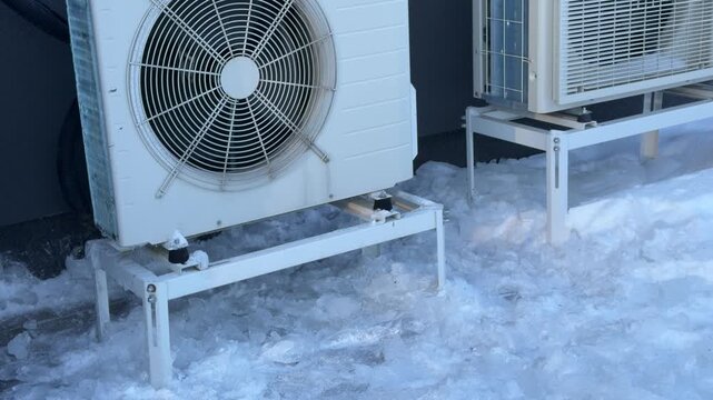 Two Heat Pump Units with Ice Buildup in Winter. A wide shot shows two side-by-side heat pumps with significant ice accumulation at their bases amidst the winter snow.