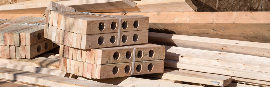 Delivered supply of lumber and bundle of vented soffit wood sections for home building job site, as a construction background
