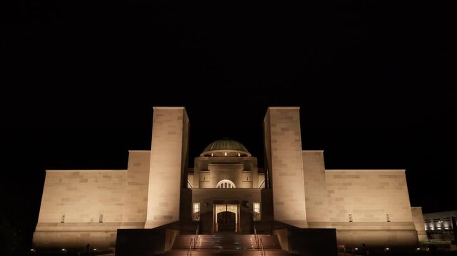 Cinematic zoom in on the iconic dome of Australian War Memorial illuminated at night in Canberra. Warm golden lighting highlights the distinctive architectural feature of this national tribute site.