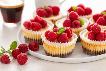 Mini cheesecakes topped with fresh raspberries on a serving plate