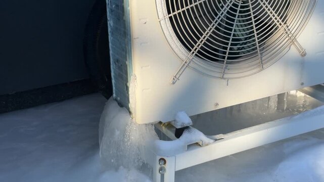 Close Up of Heat Pump Fan and Iced Base. A close-up shows a heat pump&rsquo;s fan grille and massive ice formation at the bottom, illustrating winter operation challenges in the cold.