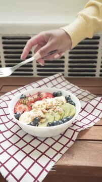 Woman Eating Healthy Fruit Bowl with Strawberries, Kiwi, Blueberries, and Bananas