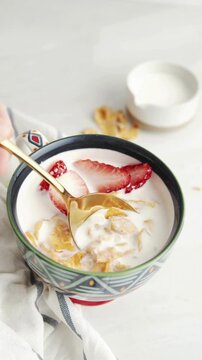 Gold Spoon Scooping Cornflakes with Milk and Fresh Strawberries in Decorative Bowl