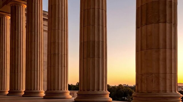 A breathtaking panoramic view showcases a majestic row of classical architectural columns bathed in the warm, golden light of either a serene sunrise or a tranquil sunset. The large, fluted pillars ri