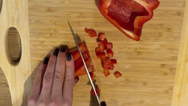 Dicing Red Bell Pepper into Small Squares. A top-down shot shows hands dicing red bell pepper strips into small, uniform squares on a wooden board, showcasing precise cutting.