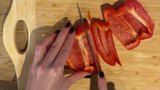 Removing the Core from a Red Bell Pepper. A top-down shot captures hands cutting a red bell pepper in half and removing the core and seeds on a wooden board for cleaning.