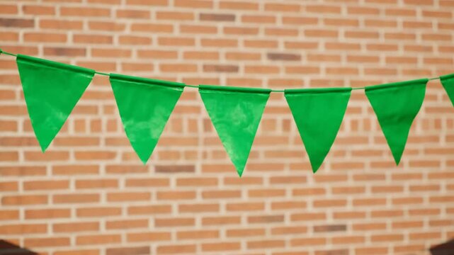 Green triangular pennant banner hanging against a brick wall background with a festive atmosphere.