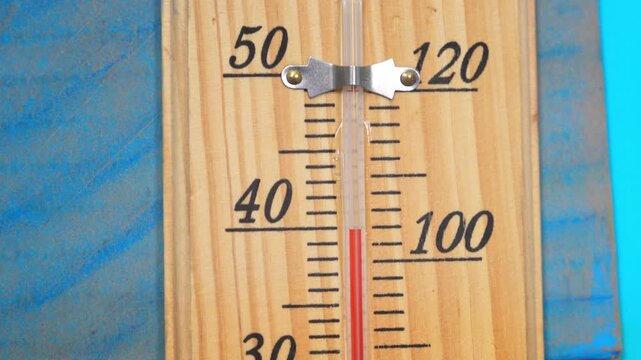 Close-up of a vertical wooden thermometer displaying temperature readings in degrees Celsius and Fahrenheit, with a red indicator on a blue background that moves upwards