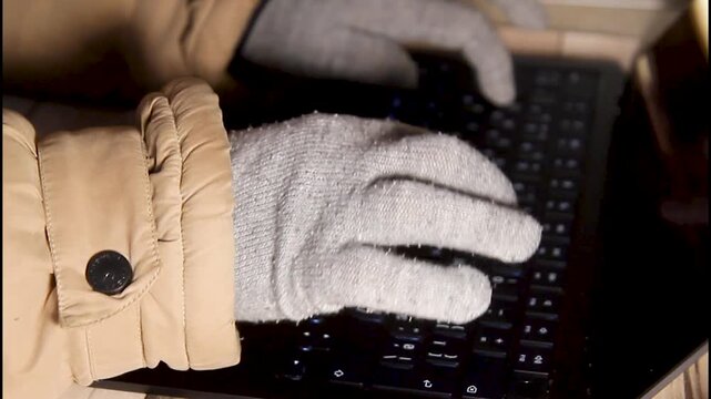 Close up top view of gloved hands working on a laptop keyboard at home during power outage and heating shutdown in winter, showing adaptation and remote work lifestyle.